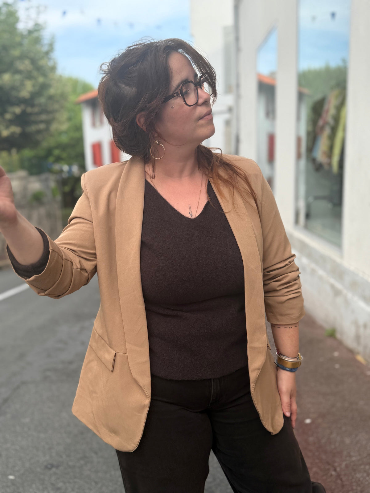 Femme portant un blazer uni camel avec un top noir et des bracelets dorés, look casual chic en extérieur