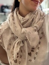 Foulard carré beige à motif bandana porté autour du cou avec une chemise blanche, format 113x113 cm, style printemps chic.