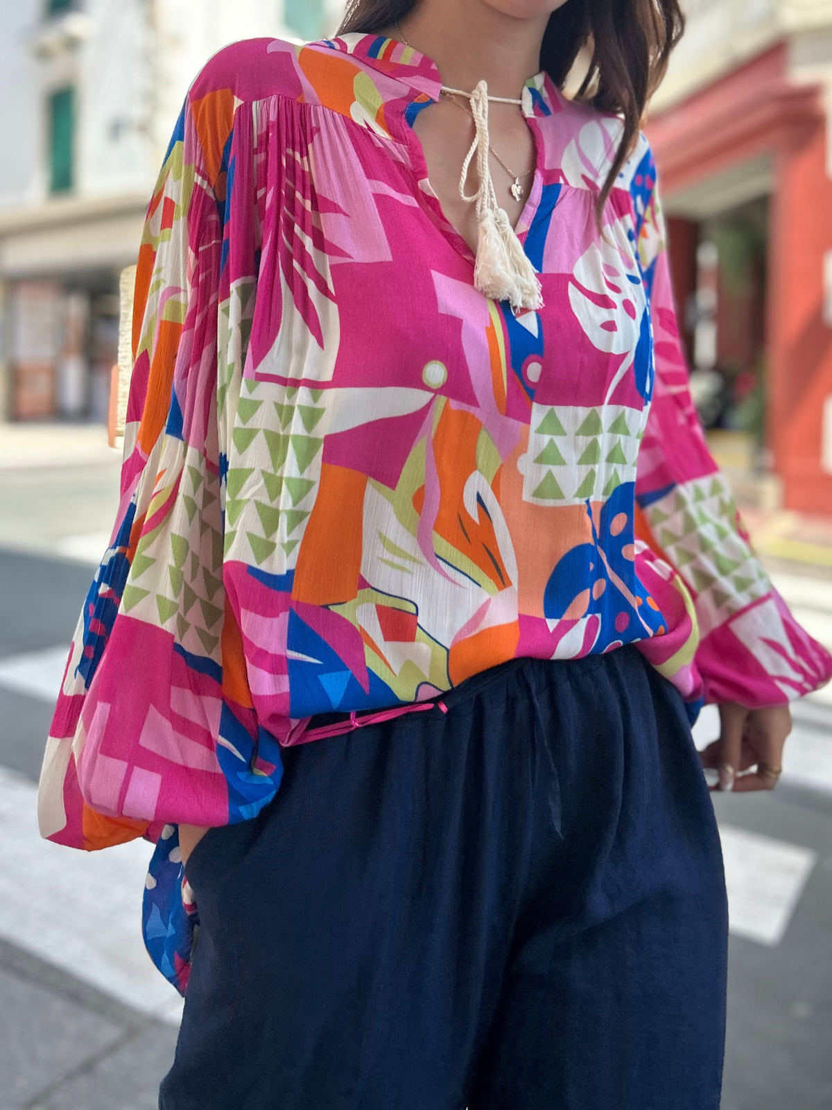 Blouse imprimé tropical manches ballon vue de face, rose fuchsia orange bleu, portée avec un pantalon large marine