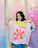 Une jeune femme souriante portant la chemise vintage "Ibiza Summer" avec des motifs vibrants et un message "Ibiza Summer Vibes". Les couleurs vives et joyeuses ressortent sur le fond rose, apportant une touche dynamique à l'ensemble.