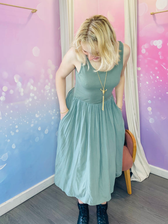 Robe sans manches à encolure ronde, de longueur mi-mollet, couleur kaki. La taille est marquée, créant un effet plissé fluide sur la jupe. Le tissu semble léger, parfait pour un look estival douc et naturel. Belle idée cadeau avec les beaux jours qui arrivent.