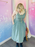 Robe sans manches à encolure ronde, de longueur mi-mollet, couleur kaki. La taille est marquée, créant un effet plissé fluide sur la jupe. Le tissu semble léger, parfait pour un look estival douc et naturel. Belle idée cadeau avec les beaux jours qui arrivent.