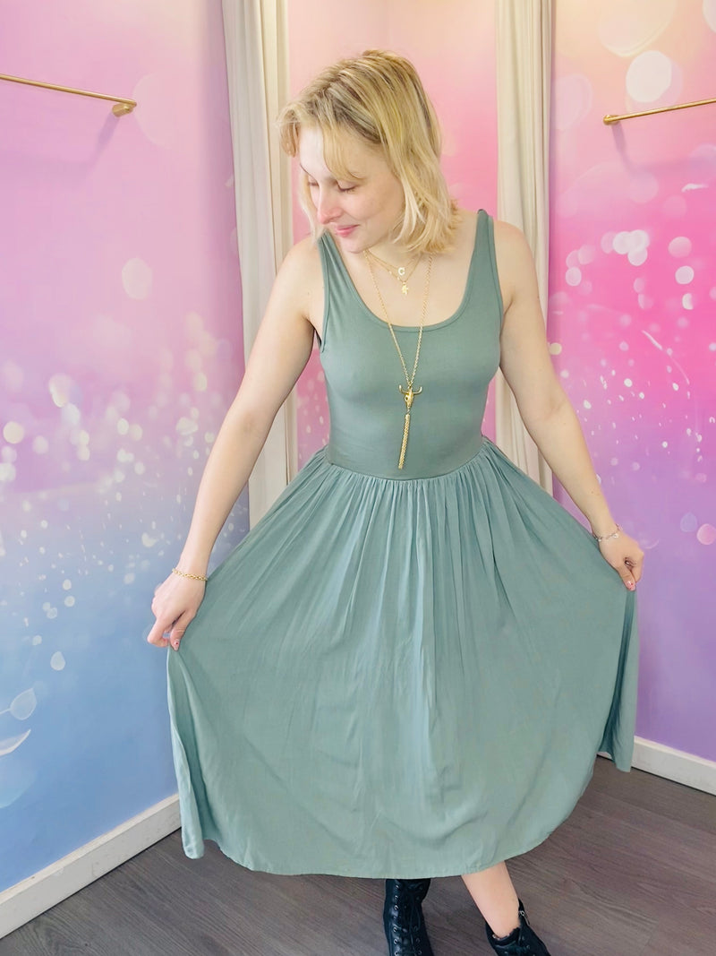 Robe sans manches à encolure ronde, de longueur mi-mollet, couleur kaki. La taille est marquée, créant un effet plissé fluide sur la jupe. Le tissu semble léger, parfait pour un look estival douc et naturel. Belle idée cadeau avec les beaux jours qui arrivent.