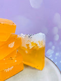 Savons artisanaux jaunes au fruit de la passion empilés, avec mousse blanche et graines de pavot, sur fond rose