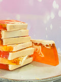 Savons artisanaux transparents orange et crème, empilés sur assiette, avec effet ruche